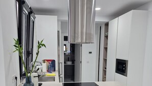 Uma cozinha moderna com ilha central, dois bancos altos, coifa de aço inoxidável e forno embutido.
