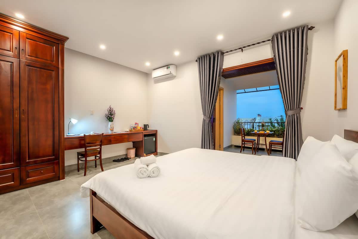 A hotel room with a large bed, a desk with a computer, a chair, and a view of the outdoors.