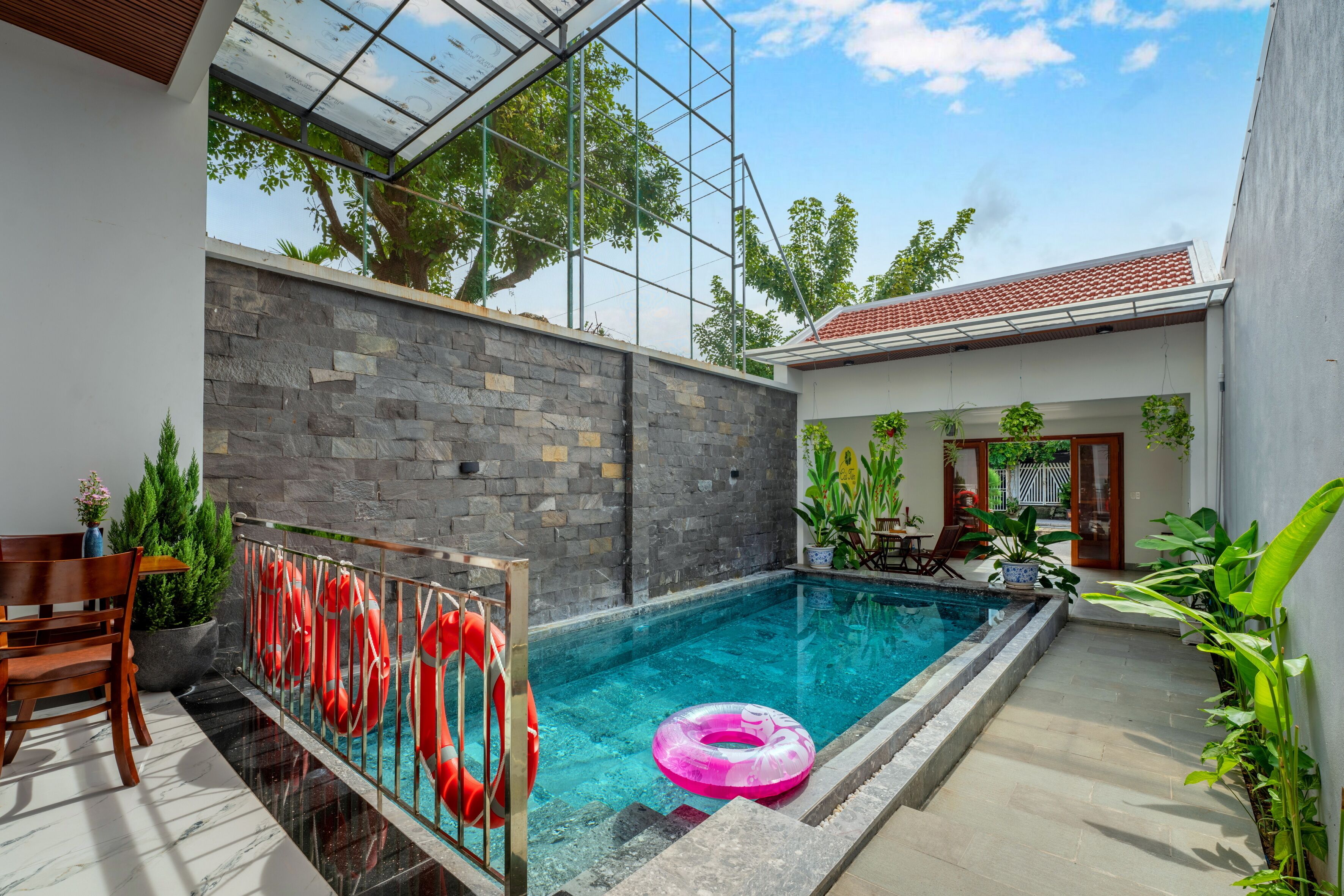 A swimming pool with a glass enclosure, surrounded by stone walls and potted plants.