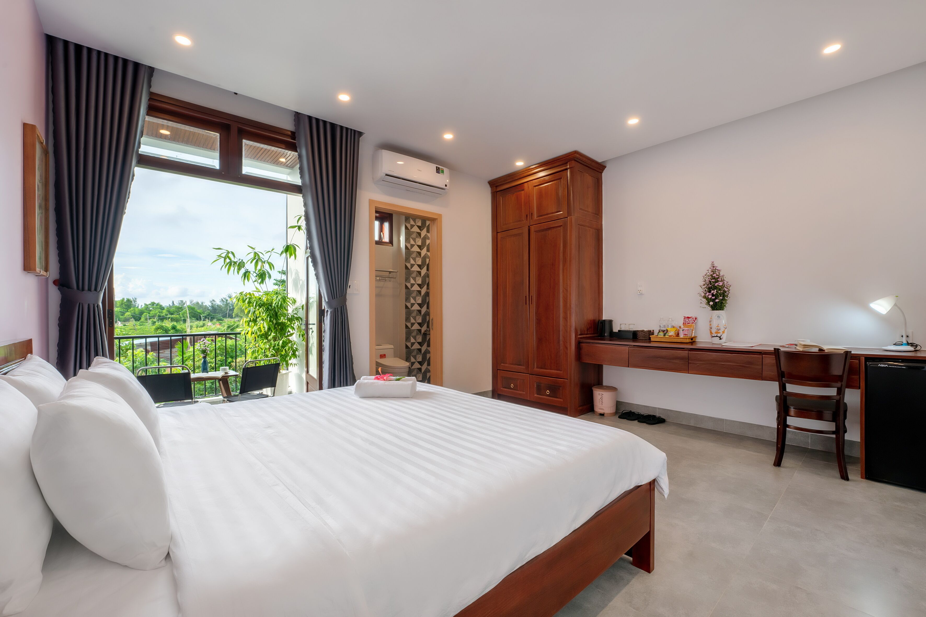 A hotel room with a large bed, a desk, and a view of greenery.