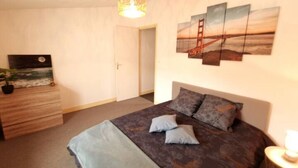 A bedroom with a bed, a dresser, a painting of a bridge, and a door.