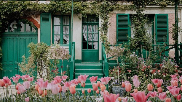 A building with green shutters and a garden with pink flowers.