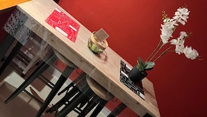 Une table à manger avec des chaises, un vase rempli de fleurs blanches et un panneau accroché au mur.
