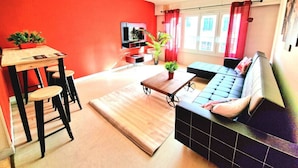 Un salon moderne avec un mur d’accent rouge, un canapé, une table basse et un coin repas avec des tabourets.