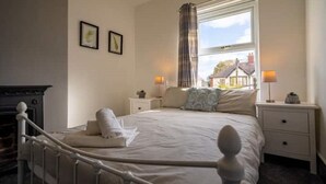 Une chambre à coucher avec un lit, deux tables de chevet, une fenêtre avec des rideaux et une cheminée.