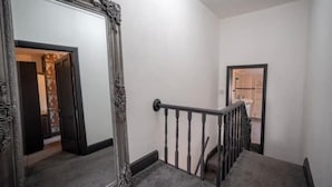 Un escalier avec une rampe noire et un grand miroir décoratif sur le côté gauche.