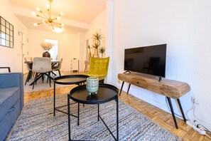 A living room with a TV, a yellow chair, a round coffee table, and a blue patterned rug.