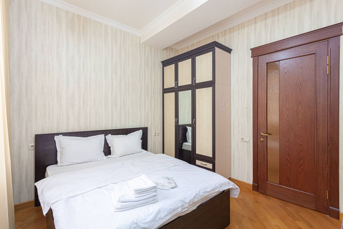 A neatly made bed with white linens, a wooden wardrobe with glass doors, and a wooden door.