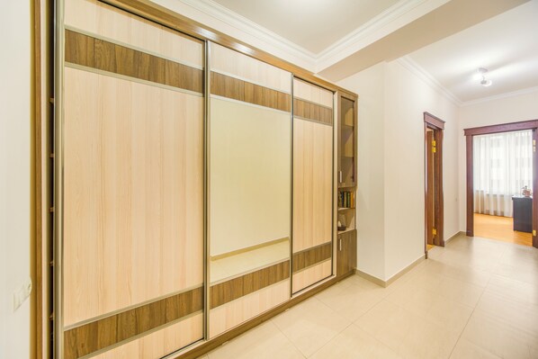 A room with a sliding wooden wardrobe, a small bookshelf, and a door leading to another room.