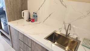 A kitchen with a marble backsplash, a stainless steel sink, and a coffee maker. - SleepRest @ NTC (Batam)