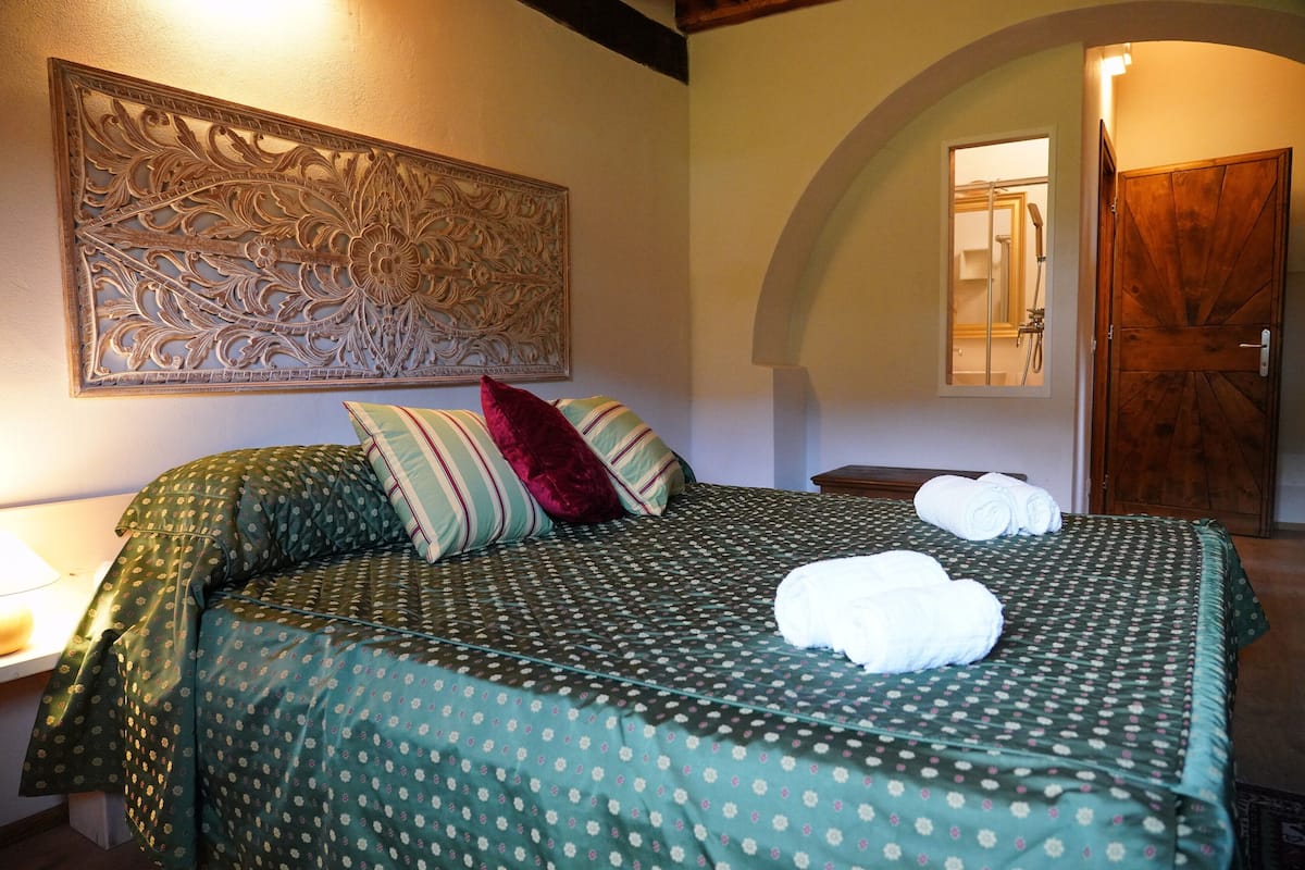 A neatly made bed with green bedding and two rolled towels, a wooden door, and a wall-mounted decorative panel.