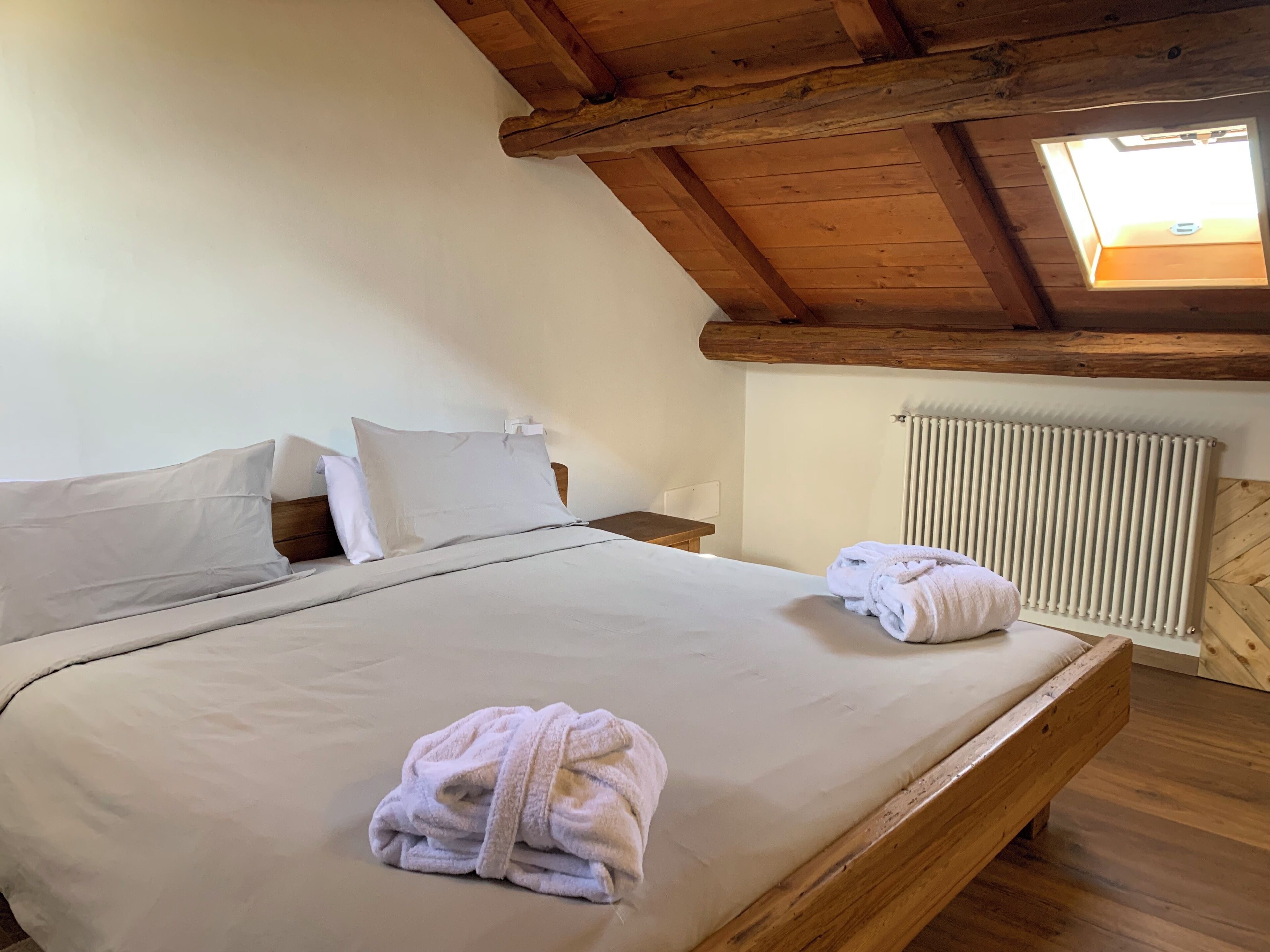 Ein Schlafzimmer mit Holzboden, einem Oberlicht, einem Bett mit weißer Bettwäsche und einer Heizung.