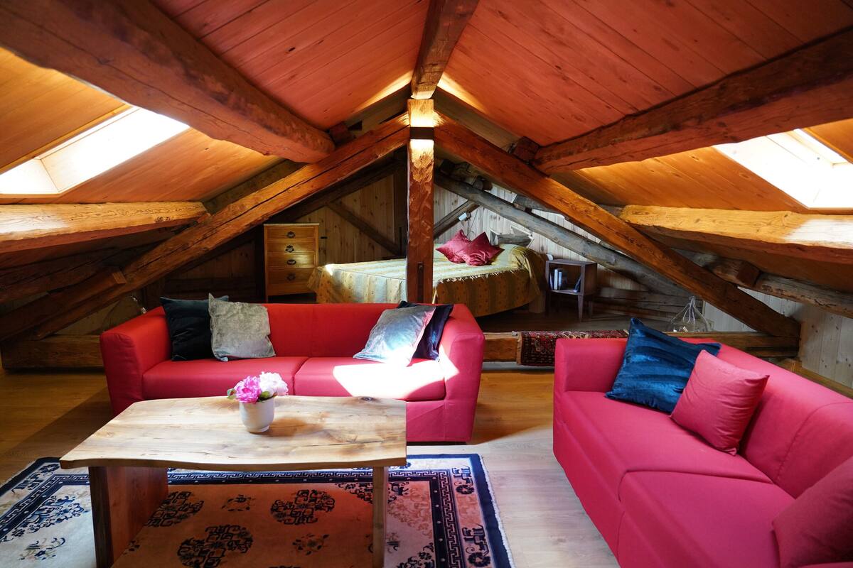 An attic bedroom with a red sofa, a wooden table, and a skylight.