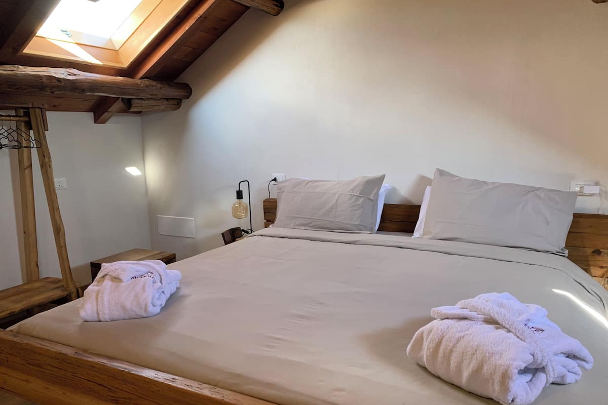 A neatly made bed with white linens and two towels, a wooden headboard, and a skylight above.