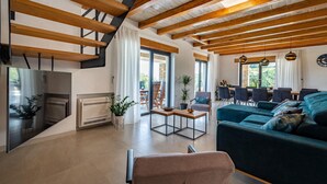 Un vaste espace de vie doté d’un plafond haut, de poutres apparentes, d’une cheminée, d’un coin repas avec des chaises et d’un canapé.