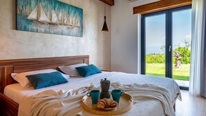 Une chambre à coucher avec un lit, des oreillers, un tableau, une machine à café, des tasses et un plateau avec des croissants.