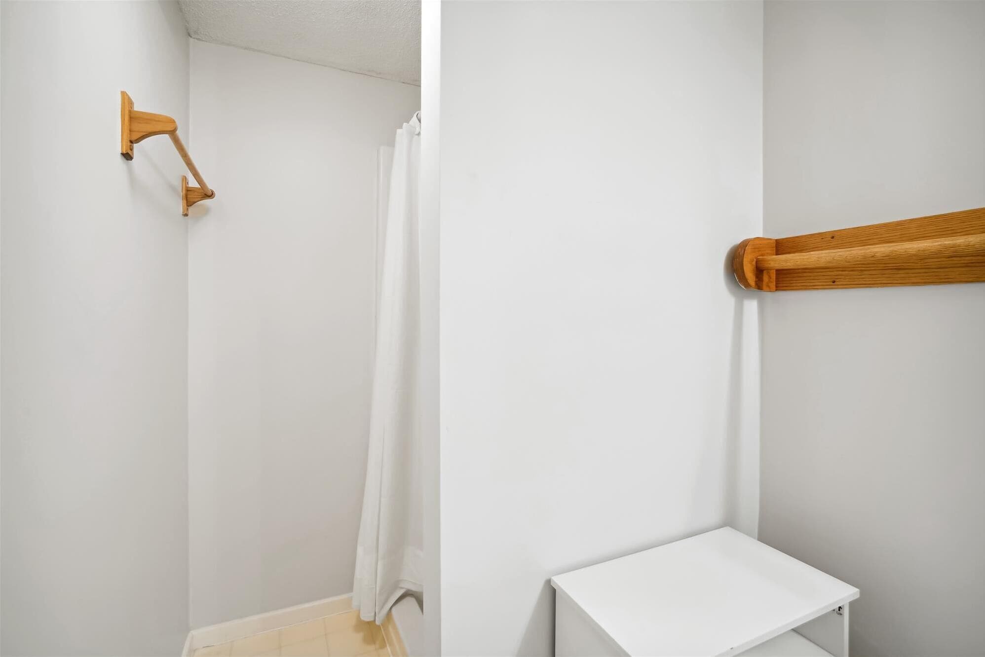 Un bagno con una doccia, un portasciugamani in legno e una piccola mensola bianca.