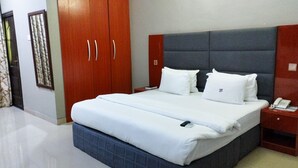 A hotel room with a large bed, a wooden wardrobe, a bedside table with a phone, and a headboard. - Breakfort Hotel and Suites (Uyo)