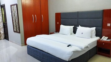 Habitación de hotel con una cama grande, un armario de madera, una mesita de noche con teléfono y un cabecero.