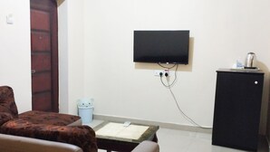A room with a sofa, a small table, a television mounted on the wall, a cabinet, and a trash bin. - Breakfort Hotel and Suites (Uyo)