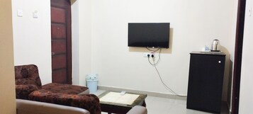 Una habitación con sofá, una mesita, televisor en la pared, armario y cubo de basura.