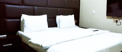 A neatly made bed with white linens and pillows, a dark brown headboard, and a bedside table with a remote control.