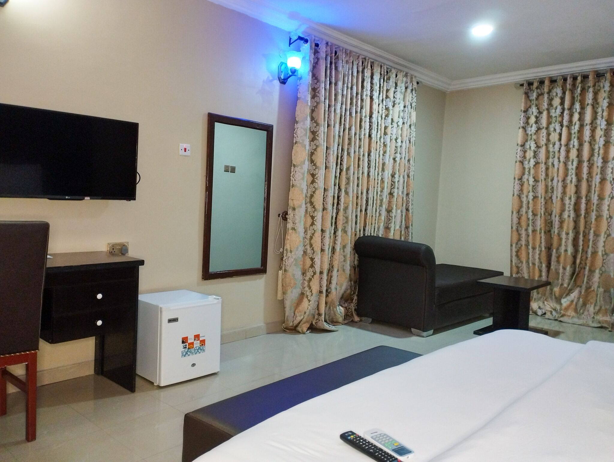 A hotel room with a bed, a desk, a chair, a television, and a small refrigerator.
