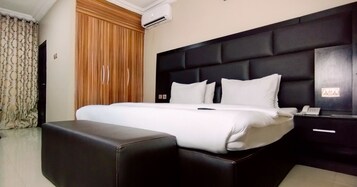 Una cama bien hecha con cabecera negra, una mesita de noche con un teléfono y un panel de pared de madera.