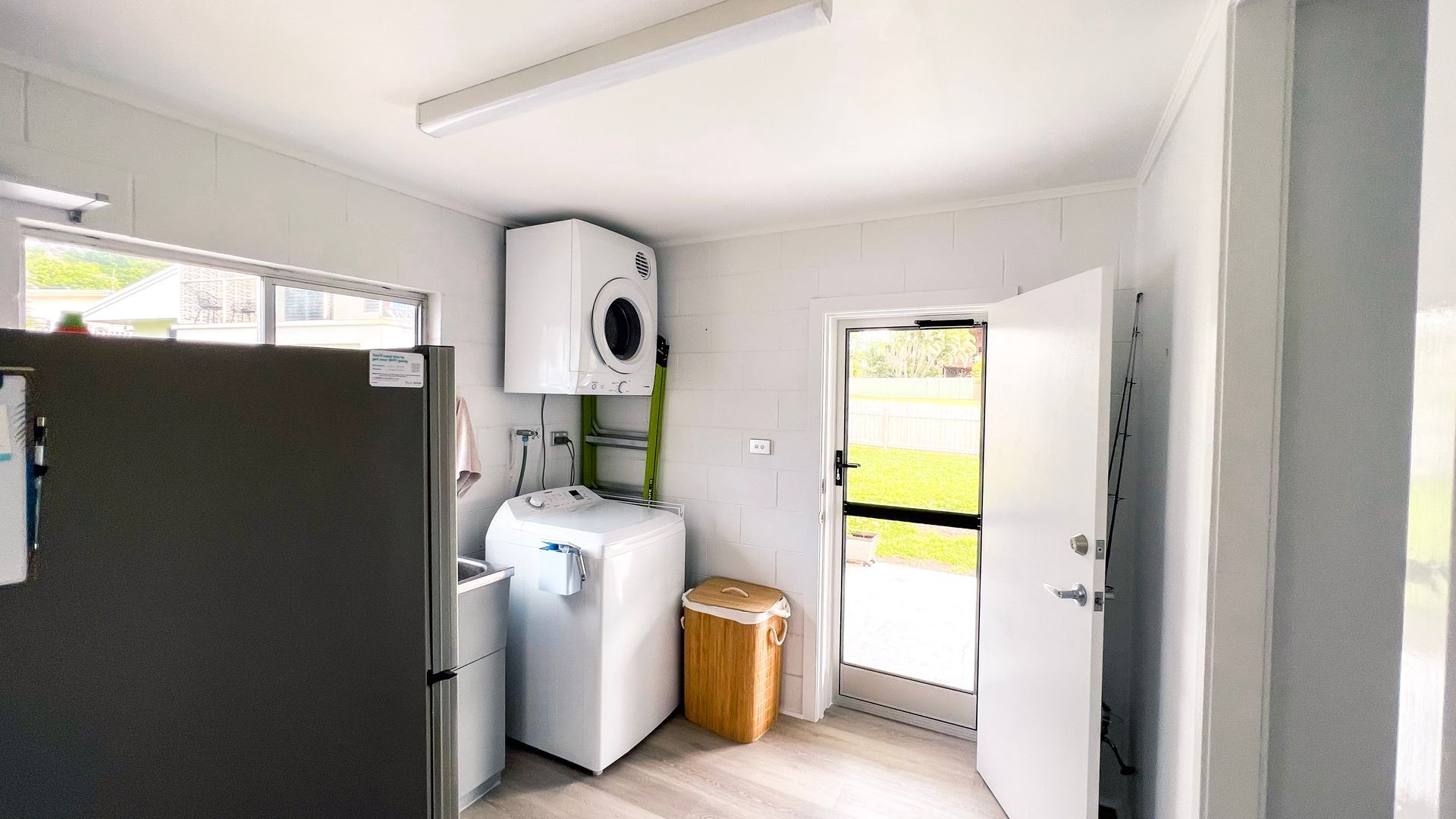 A compact kitchen with a refrigerator, washing machine, and a small trash bin.