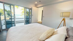 Une chambre avec un grand lit, une table de chevet, une lampe et une porte-fenêtre coulissante donnant sur un espace extérieur.