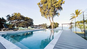 Une piscine à débordement avec des chaises longues et une terrasse en bois.