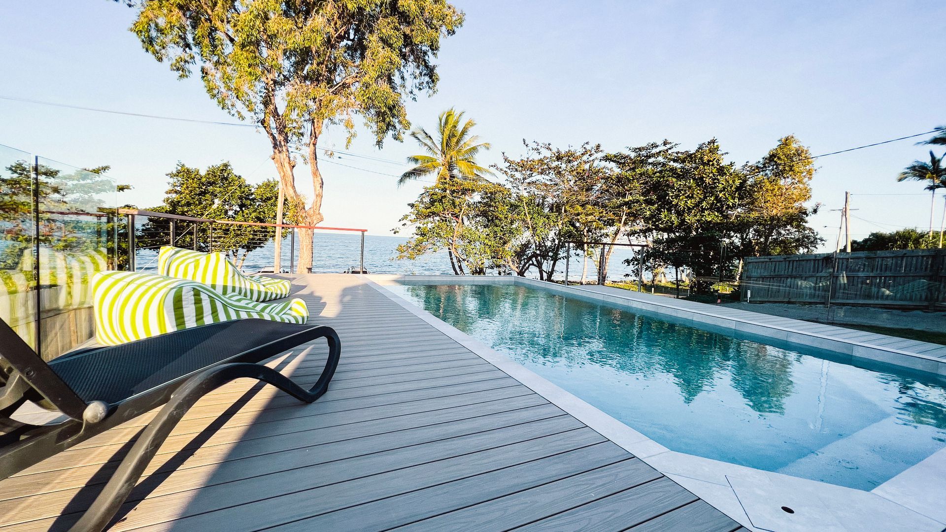 Ein Poolbereich mit Holzterrasse, Liegestühlen und Blick auf das Meer.