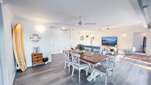 A modern living room with a dining area, a surfboard, and a TV. - Bella Luna Beach Front 2 bed (South Mission Beach)