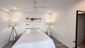 A bedroom with a bed, two bedside lamps, a ceiling fan, and a beach-themed wall art. - Bella Luna Beach Front 2 bed (South Mission Beach)