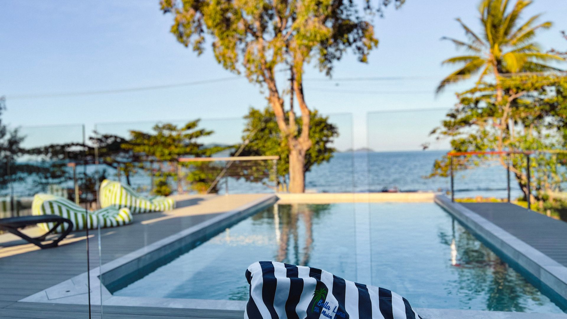A pool area with lounge chairs and a view of the sea.