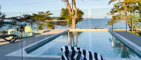 A pool area with lounge chairs and a view of the sea.