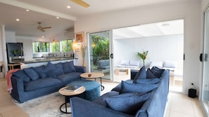 A modern living room with a sofa set, a coffee table, and a dining area with a TV and kitchen counter.