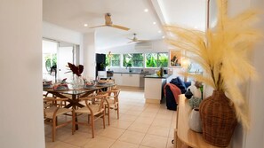 A modern kitchen with a dining area, large windows, and a ceiling fan.