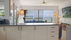 A modern kitchen with a large island, a dining area with a view of the sea, and a ceiling fan. - Tide Pool Ocean Front 2 bed (South Mission Beach)