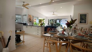 A modern kitchen with white cabinets, a dining area with a glass table, and a view of the outdoors. - Tide Pool Ocean Front 2 bed (South Mission Beach)