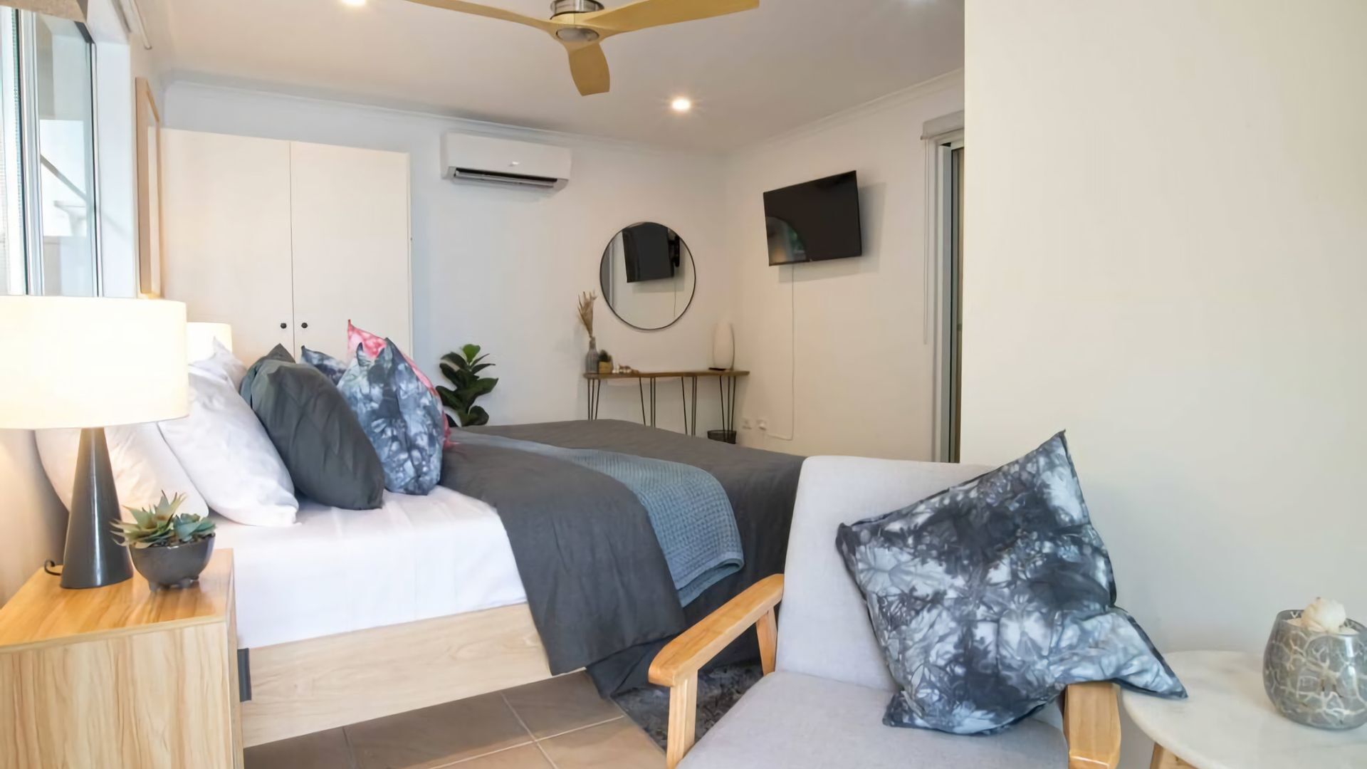 A modern bedroom with a bed, bedside table, lamp, and a small plant.