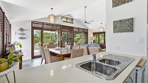 A modern kitchen with a large island, a dining area with wicker furniture, and a view of the outdoors.