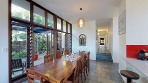 Uma área de refeições com mesa e cadeiras de madeira, grandes janelas e um lustre.
