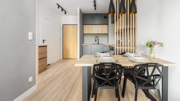 Un espace de salle à manger moderne avec une table en bois, des chaises noires et des luminaires suspendus.