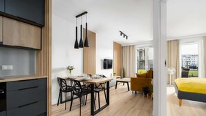 Une cuisine moderne avec des meubles en bois, un coin repas avec une table et des chaises, un canapé jaune et un lit avec une couette jaune et grise.