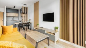 Un salon moderne comprenant un canapé, une table basse, un téléviseur et un coin cuisine avec une table à manger et des chaises.