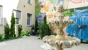 Une cour avec une fontaine en pierre, une fresque ornée de motifs floraux et un bâtiment doté de fenêtres et d’une porte.