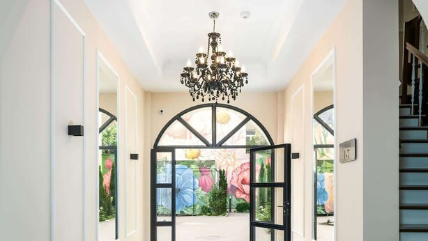 Un couloir doté d’un sol à carreaux noirs et blancs, d’un lustre et d’une vue sur un jardin, visible à travers une porte vitrée.