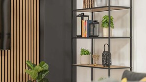 Un salon moderne avec une bibliothèque en métal noir, un mur recouvert de lambris en bois et un canapé gris.