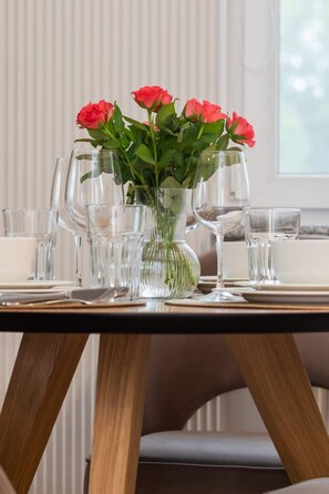 A dining table with a clear glass vase containing pink roses, surrounded by empty wine glasses and plates.